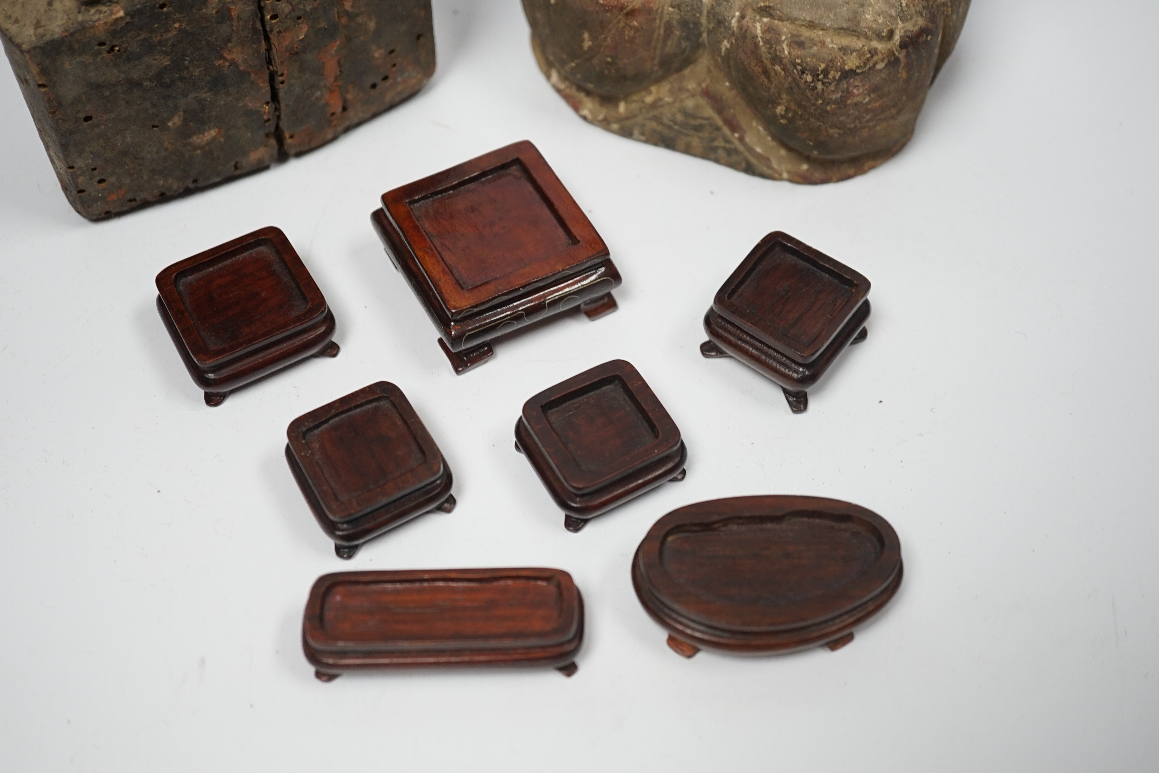 Two Chinese or Southeast Asian carved wood figures of seated immortals, and seven small wood stands, largest 24cm high